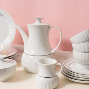 Op de afbeelding: Een witte porseleinen theeservies met zilveren rand. De set bevat een theepot, melkkan, suikerpot, borden en theekopjes. De theekopjes en suikerpot hebben een textuur van een diamantpatroon.