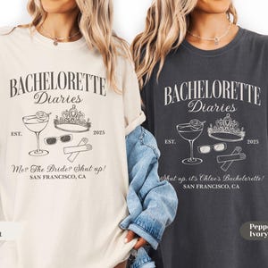 May include: Two t-shirts, one ivory and one pepper, with a graphic design. The design includes the text "BACHELORETTE Diaries", a cocktail, sunglasses, a crown, and the year 2025. The ivory shirt says "Me? The Bride? Shut up!" and the pepper shirt says "Shut up, it's Chloe's Bachelorette!"