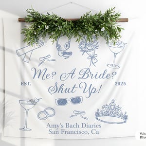 以下が含まれることがあります： 青いイラストとテキストが描かれた白い布製の壁掛け。テキストは「Me? A Bride? Shut Up!」で、王冠、サングラス、カクテルの追加テキストとイラストが描かれています。バナーは緑で飾られています。