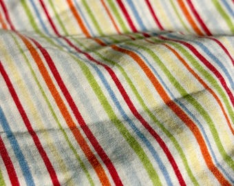 Peut inclure: Un tissu textile présentant un motif à rayures verticales répétitives dans des couleurs vives, notamment rouge, orange, vert clair et bleu clair sur un fond blanc. Le matériau est plié, créant des ondulations et des ombres naturelles.