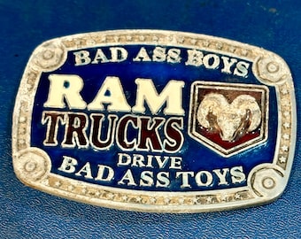 Hebilla de cinturón ovalada de metal plateado y esmalte con el logotipo de Ram Trucks y el eslogan "Bad Ass Boys Drive Bad Ass Toys" (Los chicos malos conducen juguetes malos).