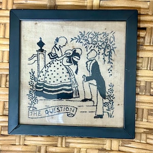 Ricamo vintage incorniciato intitolato "La domanda", raffigurante la silhouette nera di una proposta di matrimonio in stile vittoriano.