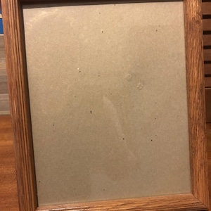 Könnte beinhalten: Ein rechteckiger Bilderrahmen aus Holz mit hellbraunem Finish. Der Rahmen hat ein geriffeltes Design an den Kanten und eine Kartonrückwand. Der Rahmen ist leer und bereit für ein Foto oder Kunstwerk.