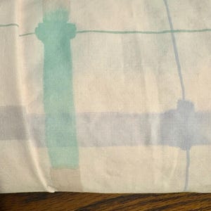 May include: A rectangular pillowcase featuring a light cream background with a grid pattern composed of intersecting horizontal and vertical lines in shades of mint green, soft blue, and muted gray, creating a subtle geometric design.