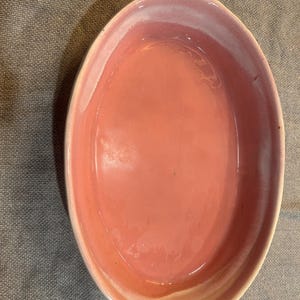 Puede incluir: Un plato ovalado de cerámica rosa con acabado brillante. El plato tiene un borde ligeramente elevado con un degradado rosa claro y blanco. El interior es de un rosa vibrante sólido.