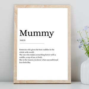 May include: A framed print with the word "Mummy" in bold black font, with a definition below. The definition describes a mother's role in providing comfort and love. A vase of flowers sits to the right.
