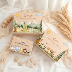 Könnte beinhalten: Drei rechteckige Holzkisten als Erinnerungsboxen mit aufgedruckten Waldtieren und Bergmotiven. Die Boxen sind mit den Namen Bastian, Leonie und Mats sowie Geburtsdatum, Uhrzeit, Körpergröße und Gewicht in Gramm personalisiert.