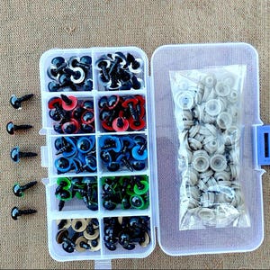 May include: A clear plastic organizer filled with various sizes and colors of doll eyes. The eyes are black, red, blue, green, and gold. A separate compartment contains white backing washers. The organizer is open on a tan surface.