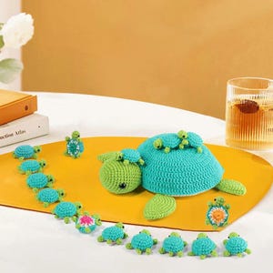 May include: A collection of handmade crochet turtles in various sizes. The large turtle is turquoise with a green head and has smaller turtles on its back. Smaller turtles are turquoise and green, arranged on a yellow surface.