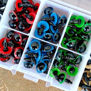 May include: A clear plastic organizer filled with colorful craft eyes. The eyes are in various colors, including red, blue, and green, with black pupils. The organizer is divided into compartments, each holding a different color of eyes, perfect for crafting and DIY projects.