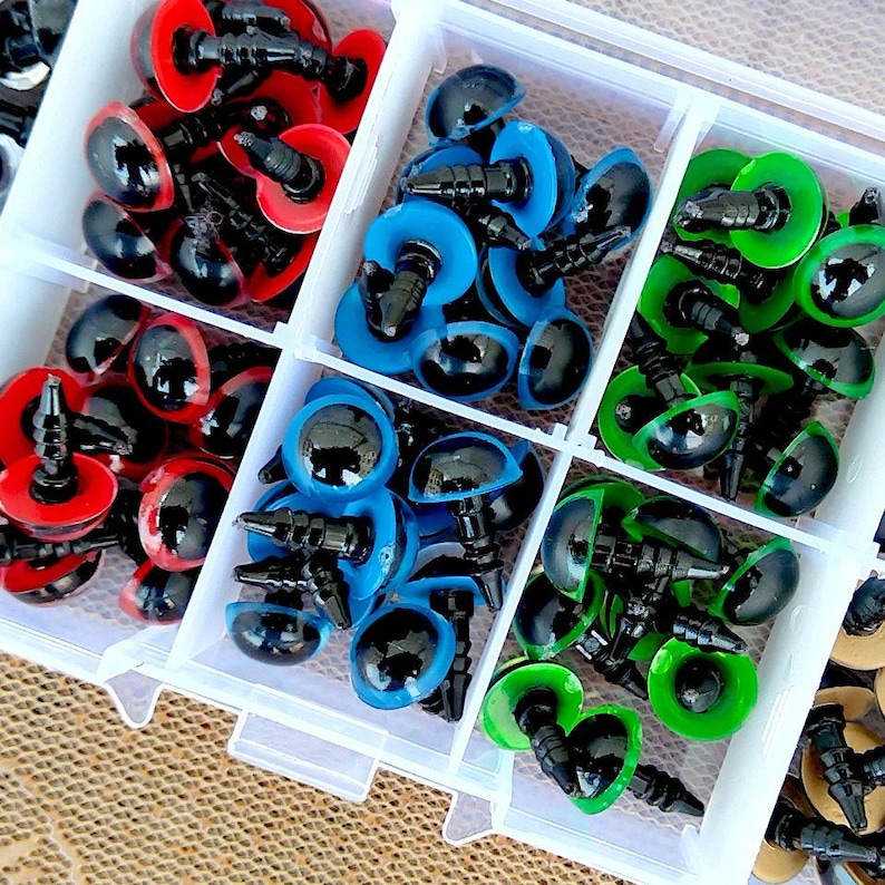 May include: A clear plastic organizer filled with colorful craft eyes. The eyes are in various colors, including red, blue, and green, with black pupils. The organizer is divided into compartments, each holding a different color of eyes, perfect for crafting and DIY projects.