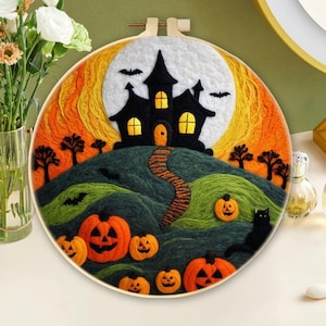 以下が含まれることがあります： ハロウィーンをテーマにした刺繍フープアート作品。黒いお化け屋敷、オレンジ色のカボチャ、黒猫、コウモリが満月とオレンジと黄色の空を背景に描かれています。このアートワークは木製のフープに額装されています。