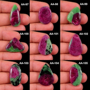 May include: A collection of nine polished ruby zoisite gemstones in various shapes including teardrop, oval, and triangular. Each stone displays a unique combination of vibrant magenta-red ruby inclusions set within a green zoisite matrix.