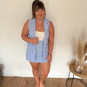 Könnte beinhalten: Ein hellblaues ärmelloses Blazer mit goldenen Knöpfen und einem passenden Rock. Das Outfit wird über einem cremefarbenen Oberteil getragen. Das Ensemble ist ein stilvolles, koordiniertes Set, perfekt für einen Sommerlook.