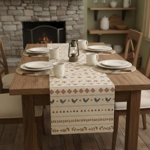 Könnte beinhalten: Ein Holztisch, gedeckt für eine Mahlzeit, mit einem gemusterten Tischläufer mit Vögeln und Sternen. Weiße Teller, Tassen und eine Laterne sind auf dem Tisch angeordnet. Gewebte Tischsets verleihen der Szene Textur.