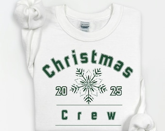 May include: White crew neck sweatshirt featuring the text "Christmas 2025 Crew" in green. A green snowflake design is between the numbers 20 and 25. The sweatshirt is neatly folded, with the sleeves rolled up.