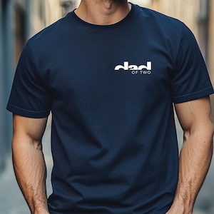 May include: Navy blue t-shirt with the white text "dad of two" printed on the chest. The shirt is a solid color and has short sleeves. The t-shirt is made of a soft material.
