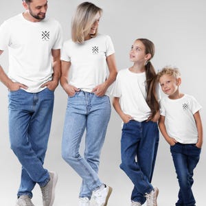 May include: Four people wearing matching white t-shirts and blue jeans. Each shirt has a small black graphic and the text "R K L E Est. 2020". The group is standing in front of a light grey background.