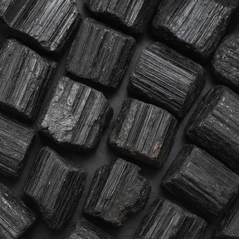 Puede incluir: Primer plano de cristales de turmalina negra en bruto. Los cristales son de un negro profundo y s&oacute;lido, con estr&iacute;as visibles y una textura natural rugosa. La disposici&oacute;n de los cristales llena el encuadre, creando una composici&oacute;n densa y rica en minerales.