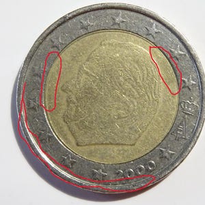 Puede incluir: Una moneda de dos euros con un centro dorado y un anillo exterior plateado. La moneda presenta un perfil de una persona en el centro dorado, rodeado de estrellas. El año 2000 es visible en el anillo plateado.