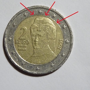 May include: A two Euro coin with a gold centre and silver outer ring. The coin features a portrait of a woman and the number "2" with the word "EURO". The year "2002" is also visible.