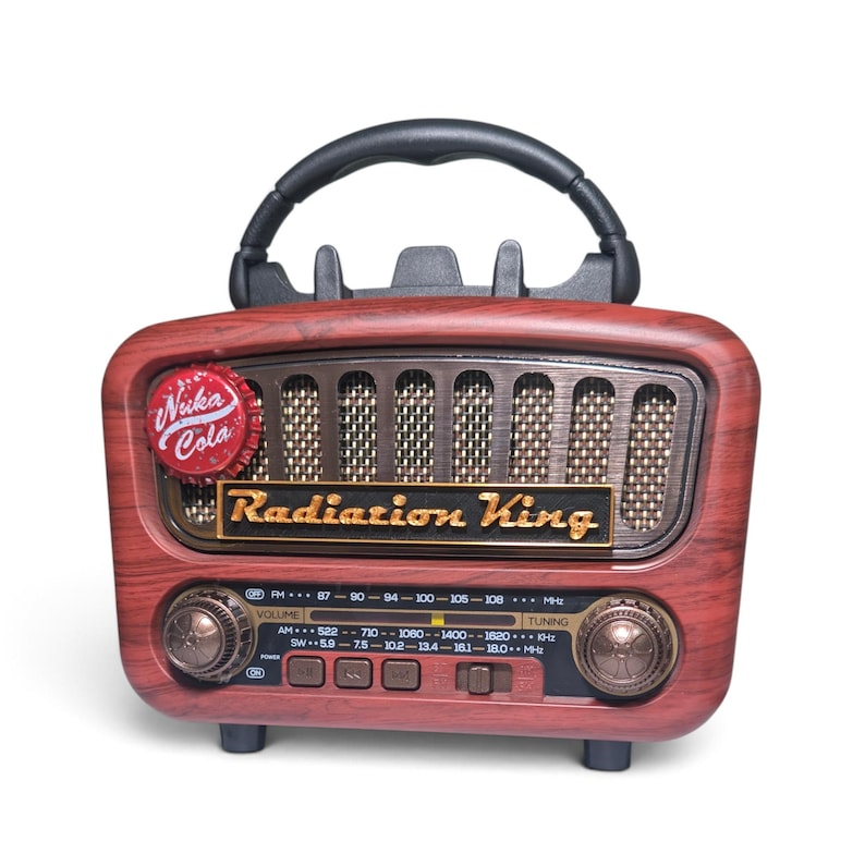 May include: A portable radio with a faux wood grain finish, featuring a black top handle and a speaker grille. The front displays a Nuka Cola bottle cap emblem, a Radiation King logo, two circular control knobs, and a frequency tuning scale.