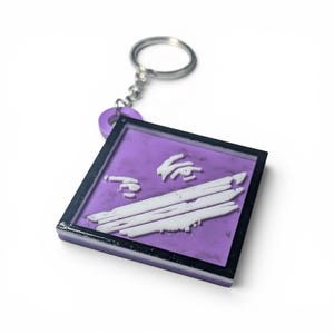 May include: A square keychain featuring a purple background with a black border and a white raised graphic design consisting of three horizontal lines and a small abstract shape above them, attached to a silver metal split ring by a purple loop.