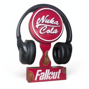 以下が含まれることがあります： 円形の看板に白い「Nuka Cola」のロゴが入った赤い木製のヘッドホンスタンド。スタンドのベースには白い文字で「Fallout」と書かれています。黒いヘッドホンがスタンドに置かれています。