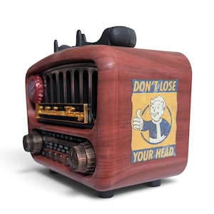 May include: A faux wood grain radio featuring a black speaker grille, two circular tuning knobs, and a red bottle cap accent. The side displays a yellow and blue graphic of a cartoon character giving a thumbs up with the text DON'T LOSE YOUR HEAD.