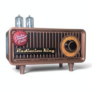 Könnte beinhalten: Ein kupferfarbenes Radio mit schwarzem Lautsprechergitter und dem Schriftzug Radiation King in goldenen Buchstaben. Ein roter Nuka Cola-Flaschenverschluss ist vorne angebracht. Zwei klare Glas-Vakuumröhren befinden sich oben auf dem Gehäuse.