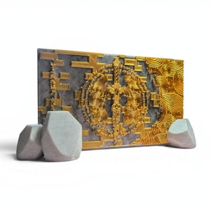 May include: A decorative wall art piece with a gold and gray color scheme. The artwork features a central gold emblem with intricate details, set against a gray background. Three light gray stone-like objects are in front of the artwork.