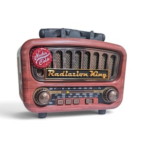 May include: A vintage-style radio with a faux wood grain finish, featuring a black handle on top and a speaker grille. The front displays a red Nuka Cola bottle cap, a gold Radiation King logo, two circular control knobs, and a frequency dial.