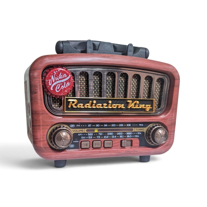 May include: A vintage-style radio with a faux wood grain finish, featuring a black handle on top and a speaker grille. The front displays a red Nuka Cola bottle cap, a gold Radiation King logo, two circular control knobs, and a frequency dial.