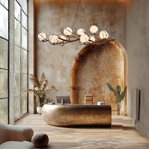 May include: An interior shot of a modern office space with a large, curved gold desk. A unique chandelier with globe lights hangs above. The room features large windows, a neutral color palette, and decorative plants.