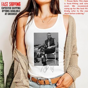 May include: White tank top featuring a black and white image of a man in a vest and sunglasses. The tank top also has the text "P-M" and a heart symbol. The words "FAST SHIPPING" and "EXPEDITED SHIPPING OPTIONS AVAILABLE AT CHECKOUT" are also visible.