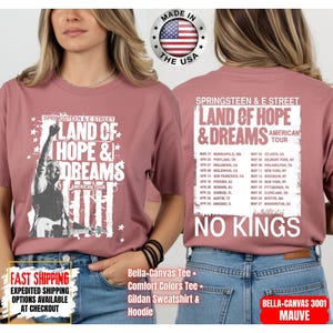 May include: Mauve Bella-Canvas tee shirt featuring a graphic of a musician with the text "Land of Hope & Dreams American Tour" and a list of tour dates. The back of the shirt also displays the tour information and the words "No Kings".