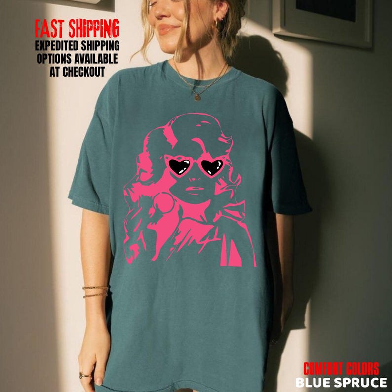 May include: Blue spruce t-shirt featuring a pink graphic of a woman wearing heart-shaped sunglasses. The text "FAST SHIPPING EXPEDITED SHIPPING OPTIONS AVAILABLE AT CHECKOUT" is printed at the top. The text "COMFORT COLORS BLUE SPRUCE" is printed at the bottom.