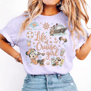 May include: A light purple t-shirt with a graphic design featuring Mickey and Minnie Mouse, a cruise ship, and the text "Life of a Cruise Girl." The design includes nautical elements like a ship's wheel, anchor, and life preserver.