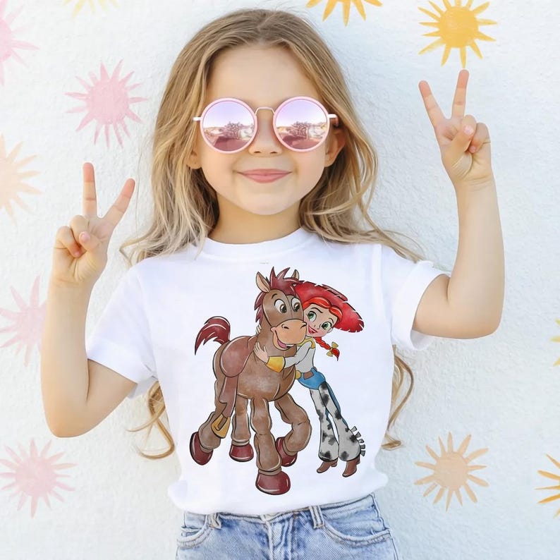 Op de afbeelding: Wit T-shirt met een cartoon illustratie van een bruin paard en een meisje met rood haar. Het meisje omhelst het paard. De afbeelding staat op een wit t-shirt.