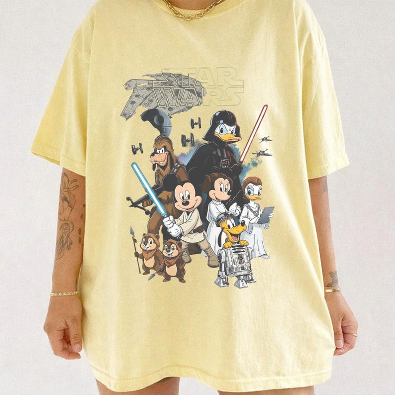 May include: Yellow t-shirt featuring a graphic of Star Wars characters and Disney characters. The design includes Darth Vader, Mickey Mouse, Donald Duck, and others. The Star Wars logo is at the top.