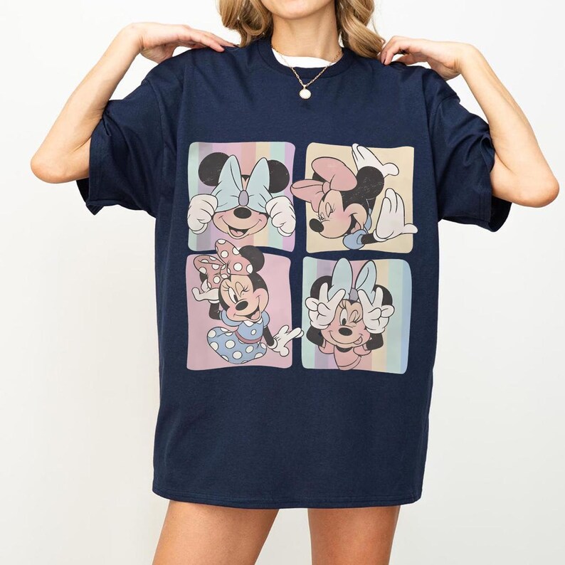 May include: Navy blue t-shirt featuring a four-panel graphic of Minnie Mouse in various poses. Each panel has a pastel background with vertical stripes. Minnie Mouse is wearing bows and dresses in the graphic.