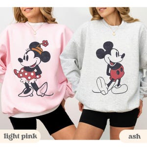 May include: Two sweatshirts, one light pink and one ash, each featuring a classic cartoon character. The light pink sweatshirt has a Minnie Mouse graphic, while the ash sweatshirt displays Mickey Mouse. The text "light pink" and "ash" are at the bottom.