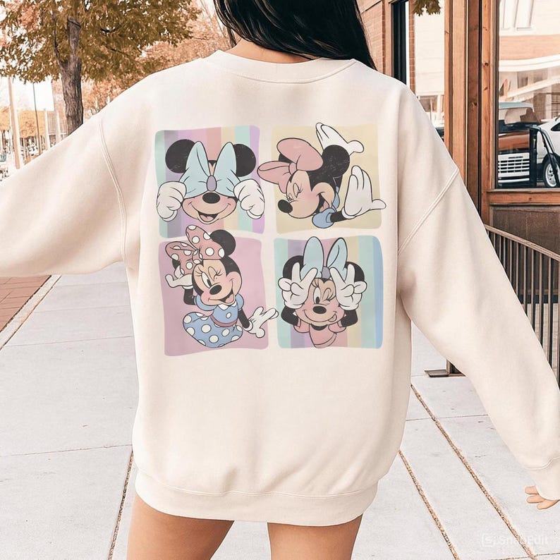 May include: Cream-colored sweatshirt featuring a colorful graphic of Minnie Mouse in four different poses. Each image is set within a pastel-colored square. The design includes Minnie's signature bow and polka dots.