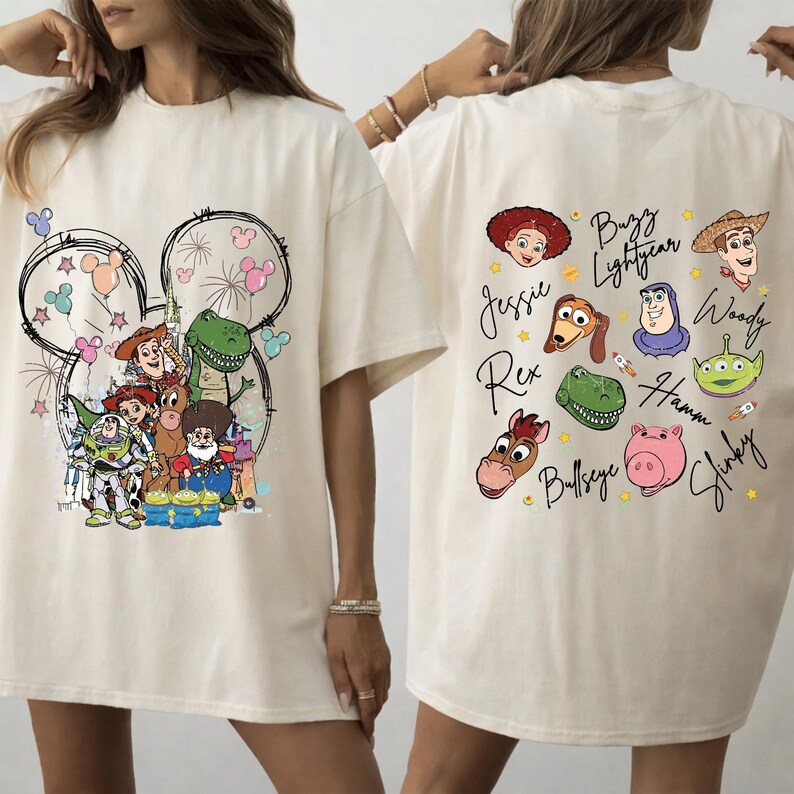 May include: Cream-colored t-shirt featuring a colorful graphic of Toy Story characters, including Woody, Buzz Lightyear, and Rex. The back of the shirt displays individual character portraits with their names. The design is set against a Mickey Mouse silhouette.