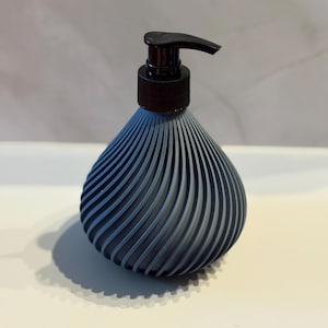 May include: A dark blue, teardrop-shaped soap dispenser with a black pump. The dispenser has a ribbed, textured design. The pump is black and has a curved spout. The dispenser sits on a white surface.