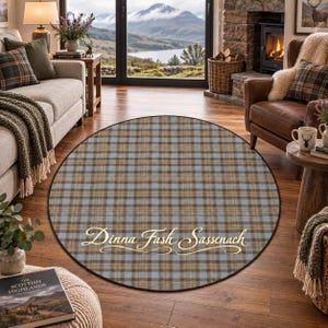 May include: A round area rug featuring a tan, brown, and light blue plaid pattern. The rug has a dark border and displays the text Dinna Fash Sassenach in a cursive, light-colored font across the center of the circular surface.