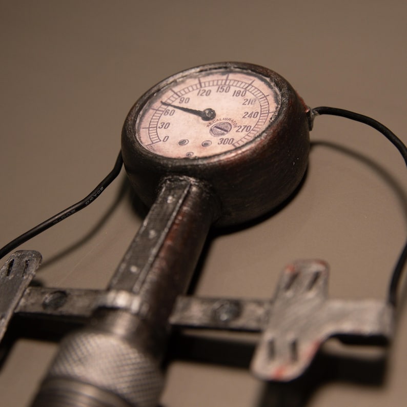 May include: Close-up of a vintage pressure gauge with a circular face and a needle pointing to 60. The gauge has a brown metal casing and a white face with black numbers. The gauge is attached to a metal handle and a clamp.