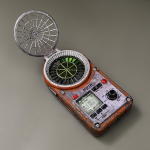 Puede incluir: Un dispositivo portátil desgastado, naranja y gris, con una cubierta articulada en forma de telaraña. El dispositivo presenta una pantalla circular con elementos verdes y negros, una pequeña pantalla que muestra datos y varios botones y un dial. El texto "BEДИГЬ" es visible.