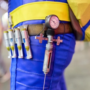 May include: A blue and yellow costume with a utility belt featuring a pressure gauge and several silver vials. The belt is brown with a yellow stripe. The costume is blue with yellow accents.