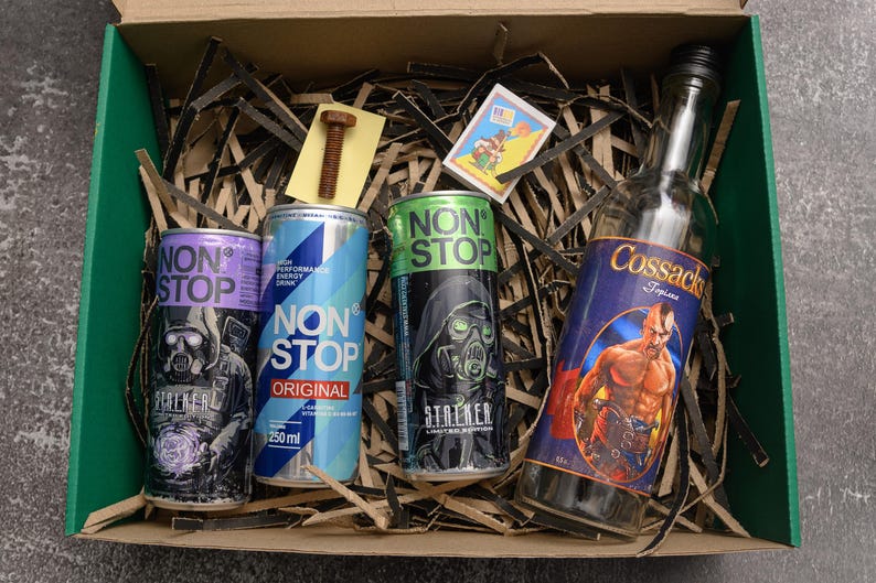 May include: A gift box containing energy drinks and a bottle of liquor. The energy drinks are in purple, blue, and green cans, with the text "NON STOP" and "STREKER". The liquor bottle has a label with a muscular man.